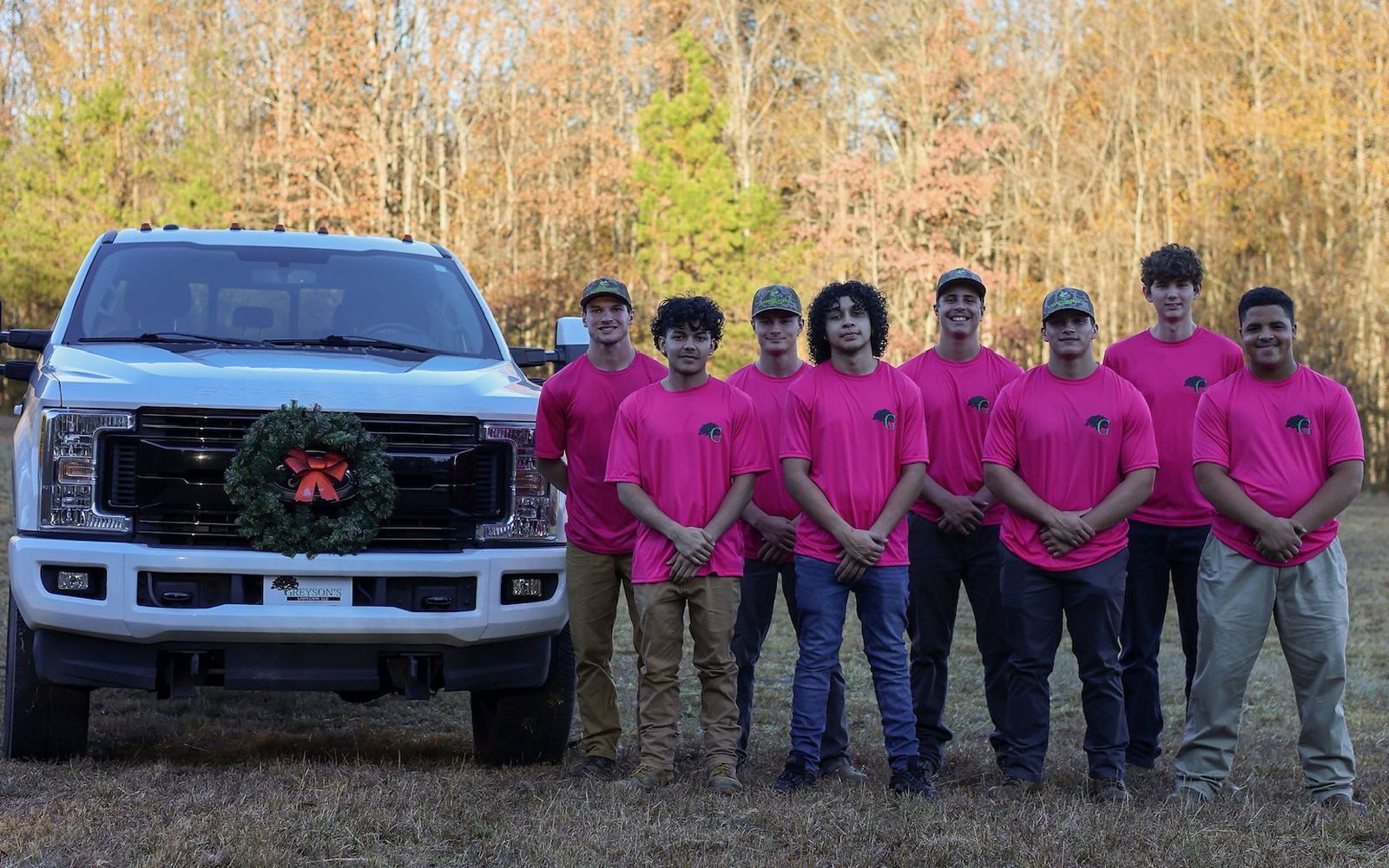 The Greyson&rsquo;s Lawn and Landscape crew lined up in matching fuchsia shirts in front of their trucks.