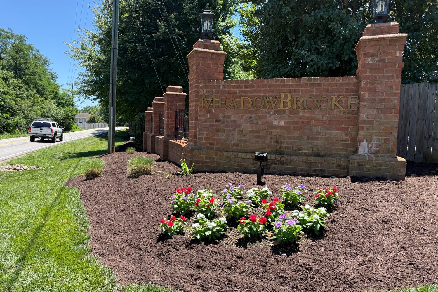 A brick neighborhood entrance monument with a fresh flower bed and mulched border.