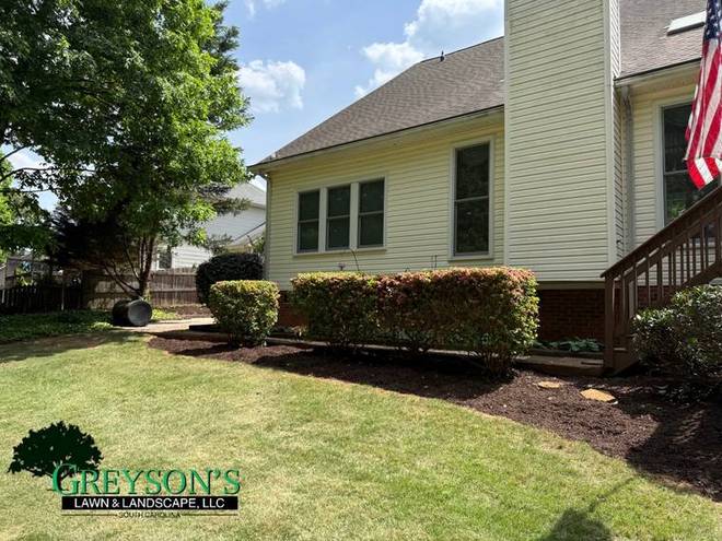 A sweeping mulch bed curve cut into a lawn beside a house.