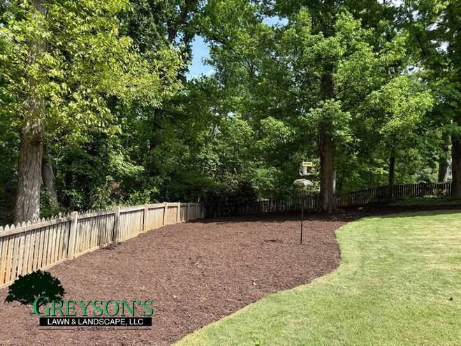 A long mulch border following a fence line across a garden.