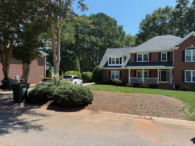 A maintained front landscape with crepe myrtles and mulched beds at a brick home.