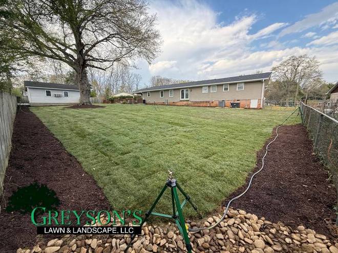 After: fresh sod laid with a new mulch bed along the fence line.
