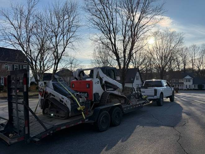 A skid steer loaded on a trailer at a job site.