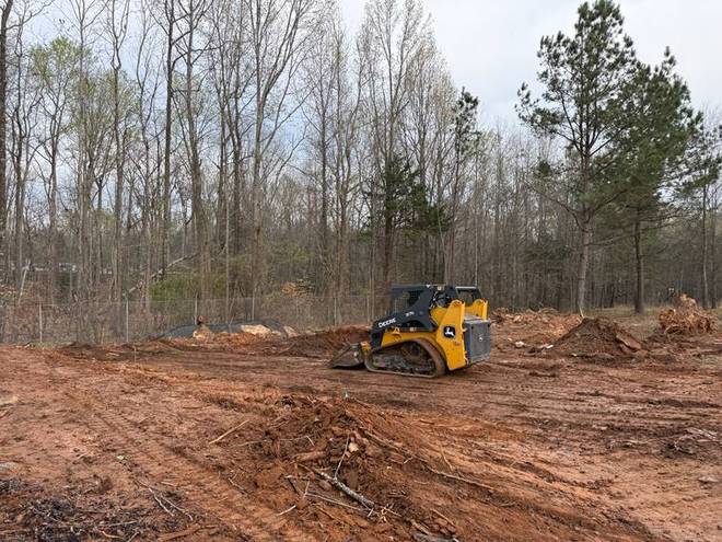 A skid steer grading bare earth on a cleared site.