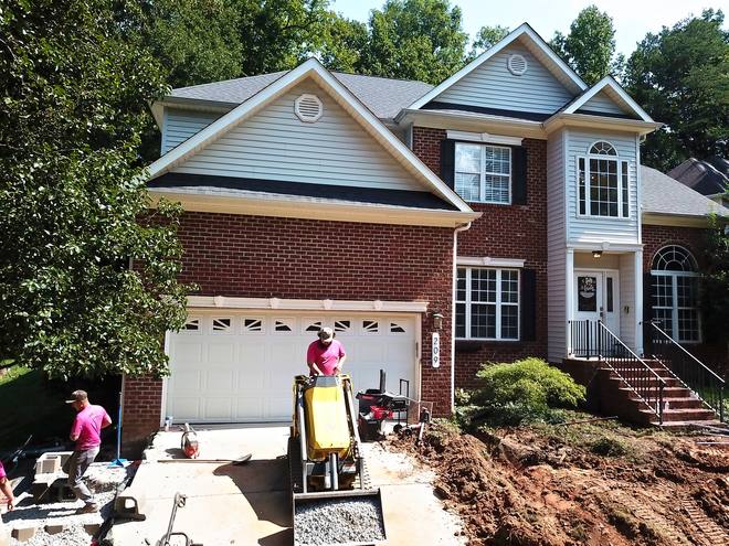 Crew and a compact loader excavating the front of a brick home, seen from above.