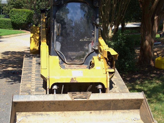 A compact track loader parked head-on in a driveway, ready for the day.