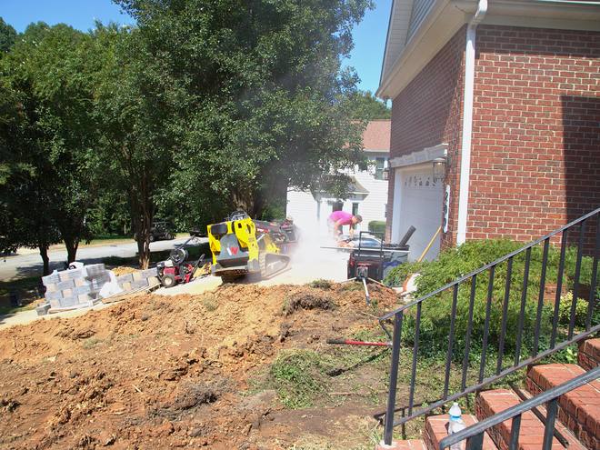 A compact loader working a trench with dust rising around it.