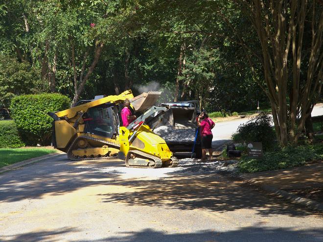 A compact track loader working along a tree-lined street.