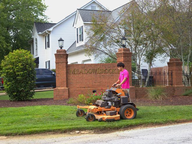 A crew member mowing in front of a neighborhood entrance wall.