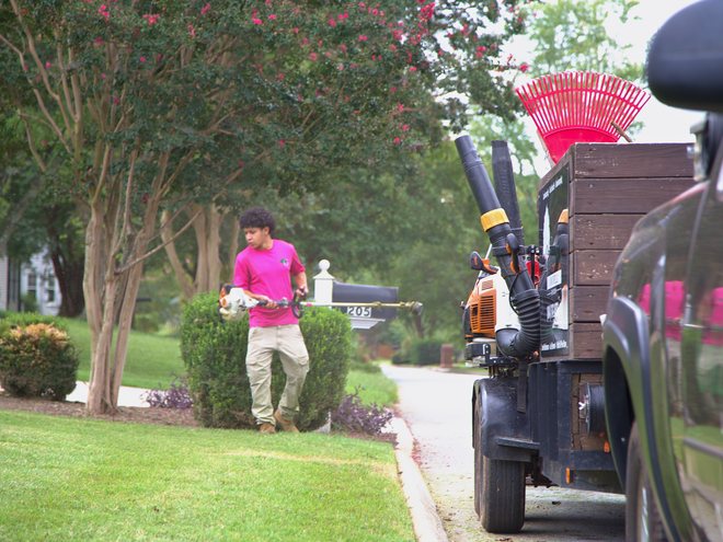 A crew member carrying a string trimmer past the company trailer.