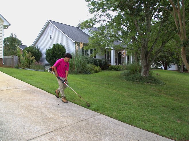 A crew member edging along a sidewalk with a string trimmer.