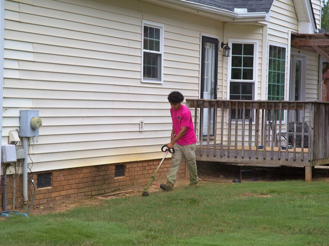A crew member trimming along the foundation of a house.