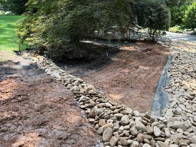 A river rock channel under construction across a back yard.