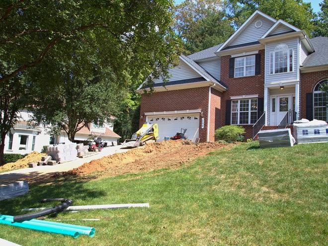 Green drainage pipe staged on the lawn in front of a brick home.