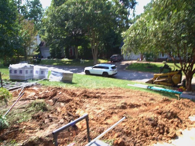 A drainage trench cut across a front yard under shade trees.