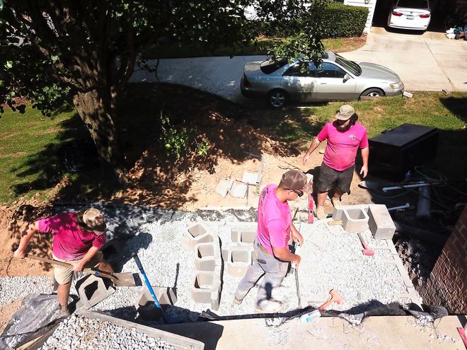 Two crew members leveling wall block on a compacted gravel base next to a garage.