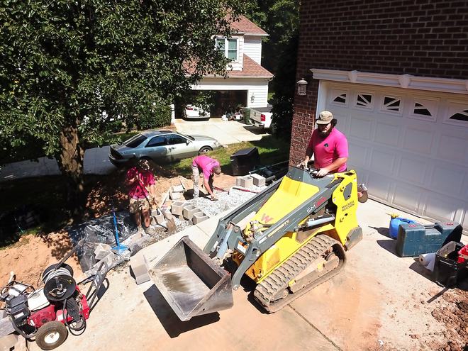 A compact track loader carrying wall block to the crew at a garage.