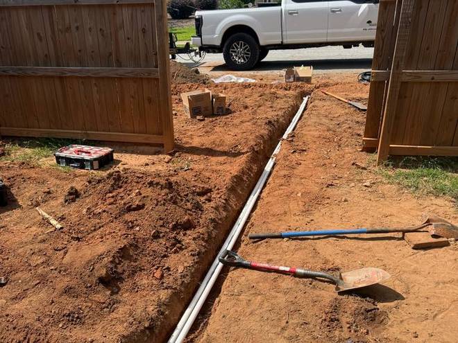 Irrigation pipe laid into an open trench beside a fence.