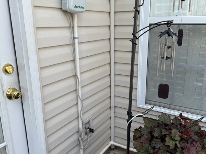 A Rain Bird irrigation controller mounted on the side of a house.