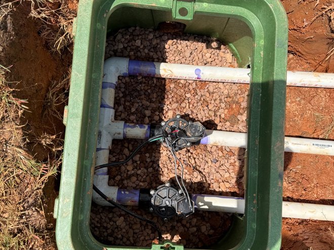 A finished irrigation valve manifold set in a gravel-bedded box.