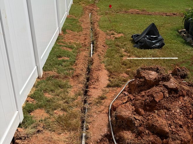 A trenched mainline with new irrigation pipe laid in it running along a fence line.