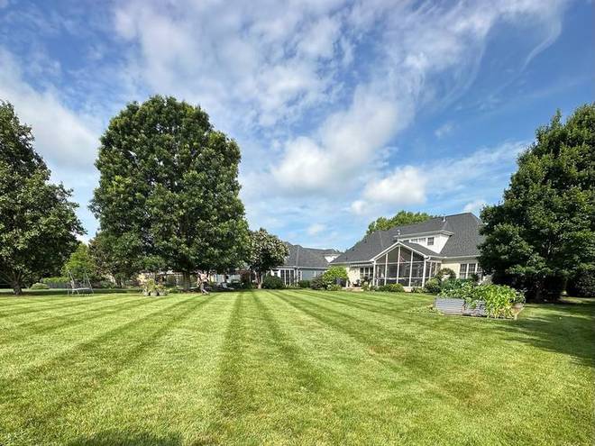 A large striped lawn with mature trees and a home behind it.