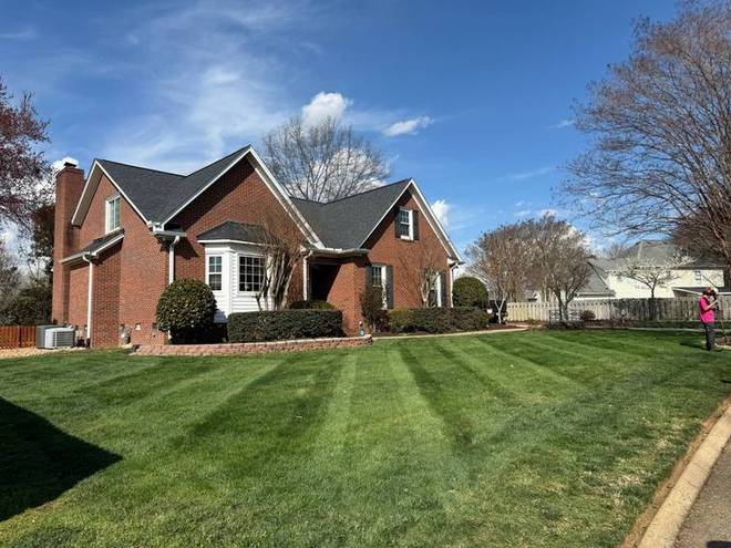 A striped front lawn running up to a brick home.