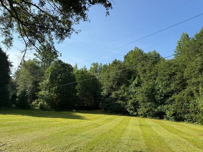 A large open lawn cut with wide mowing stripes against a tree line.