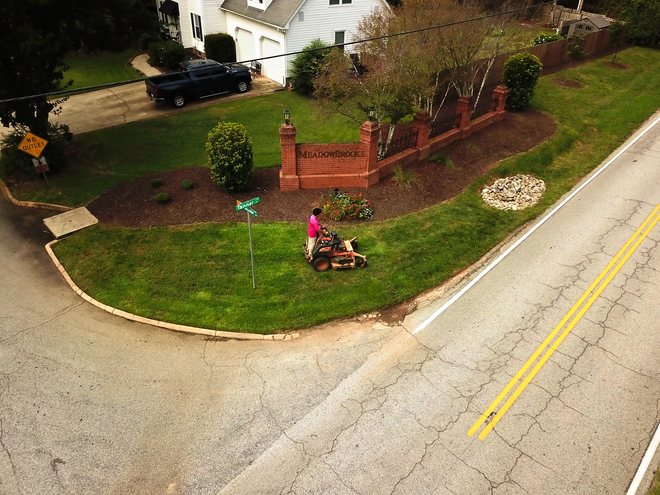 Aerial view of mowing along a brick entrance wall beside the road.