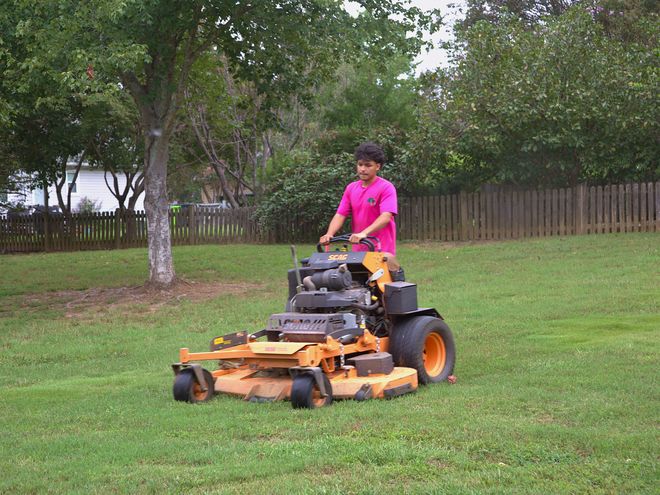 A crew member mowing a back lawn on a stand-on mower.