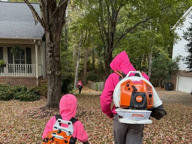 Two crew members clearing a leaf-covered yard with backpack blowers.