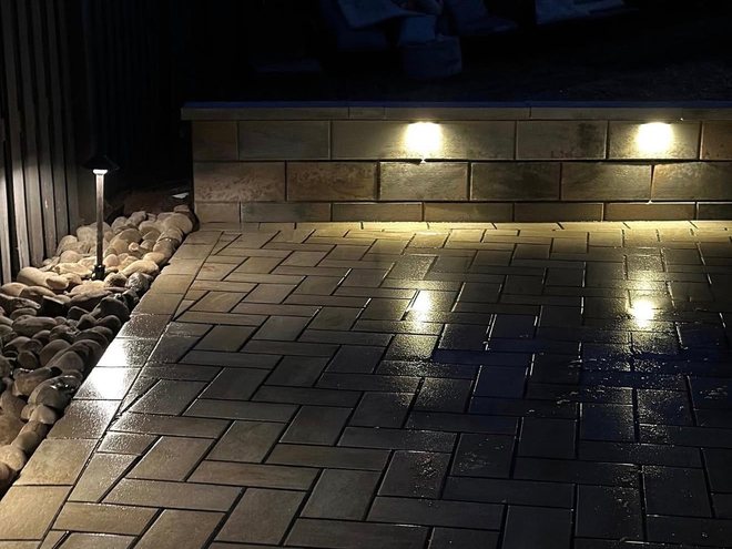 Lights set into a seating wall throwing pools of light across a paver patio.