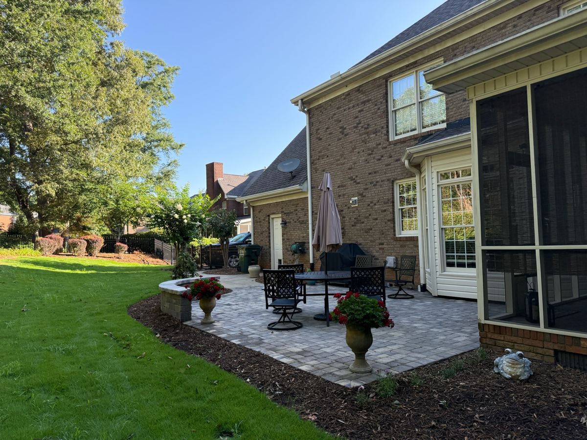 A paver patio with outdoor furniture beside a finished back lawn at a brick home.