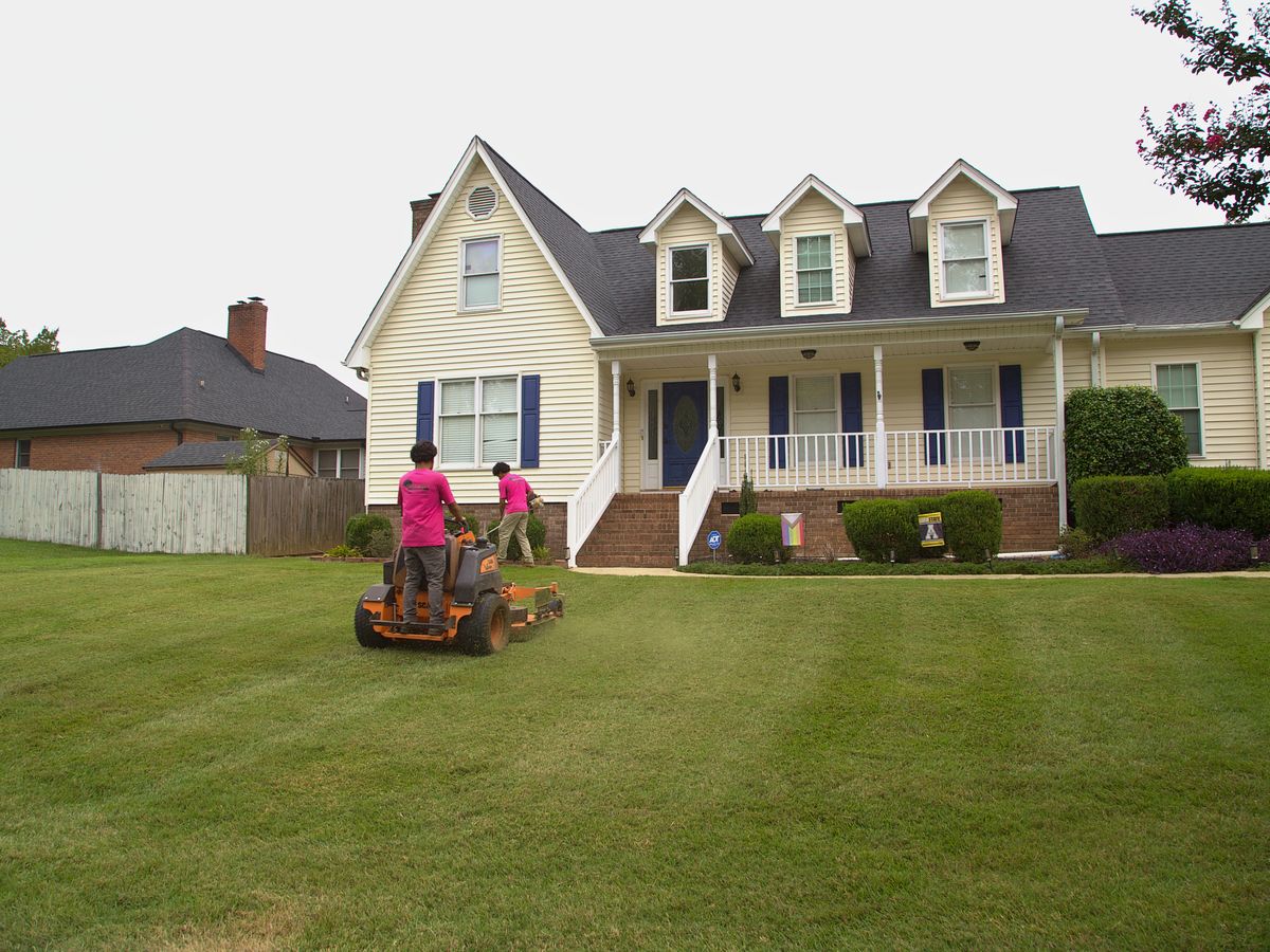 Two crew members mowing and trimming a striped front lawn.