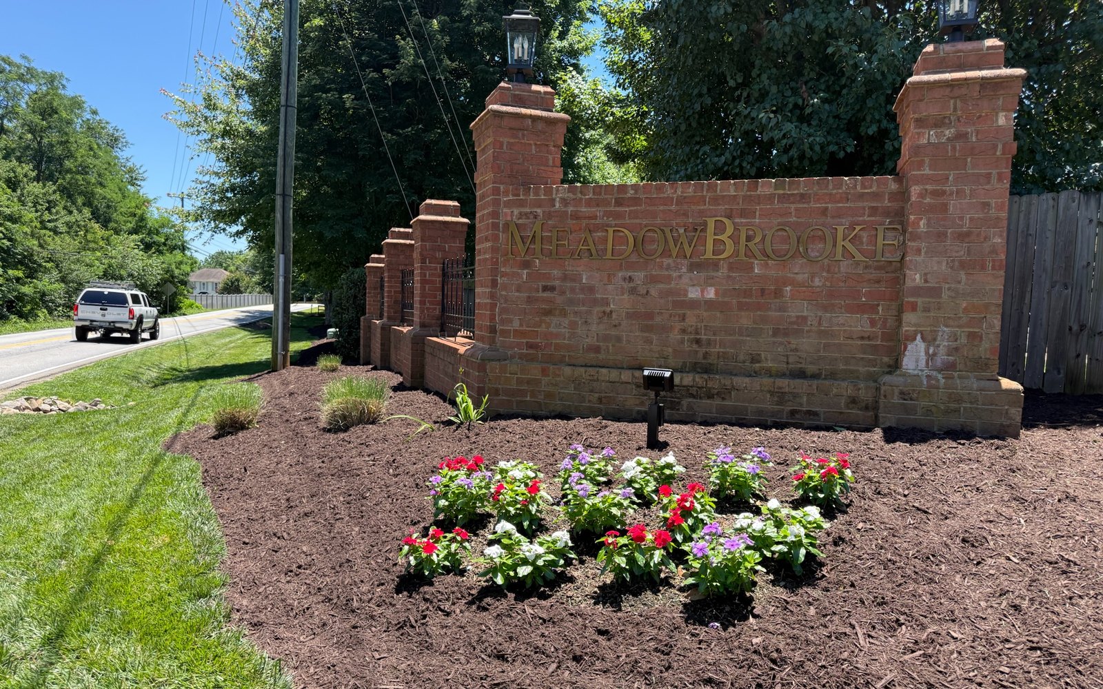 A brick HOA entrance monument with a freshly planted and mulched bed at the roadside.