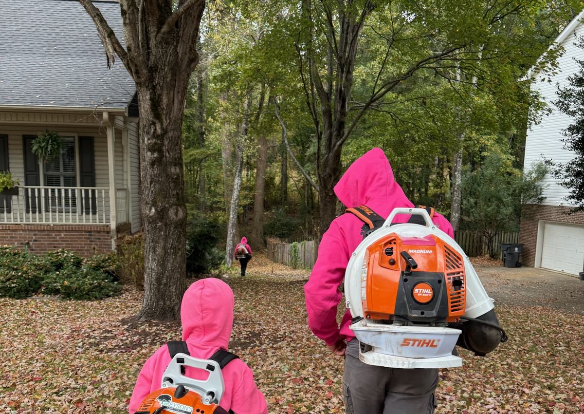 Two crew members clearing a leaf-covered yard with backpack blowers.