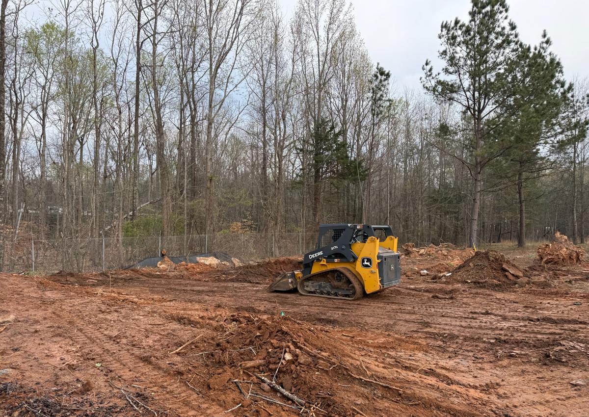 A skid steer grading bare earth on a cleared site.