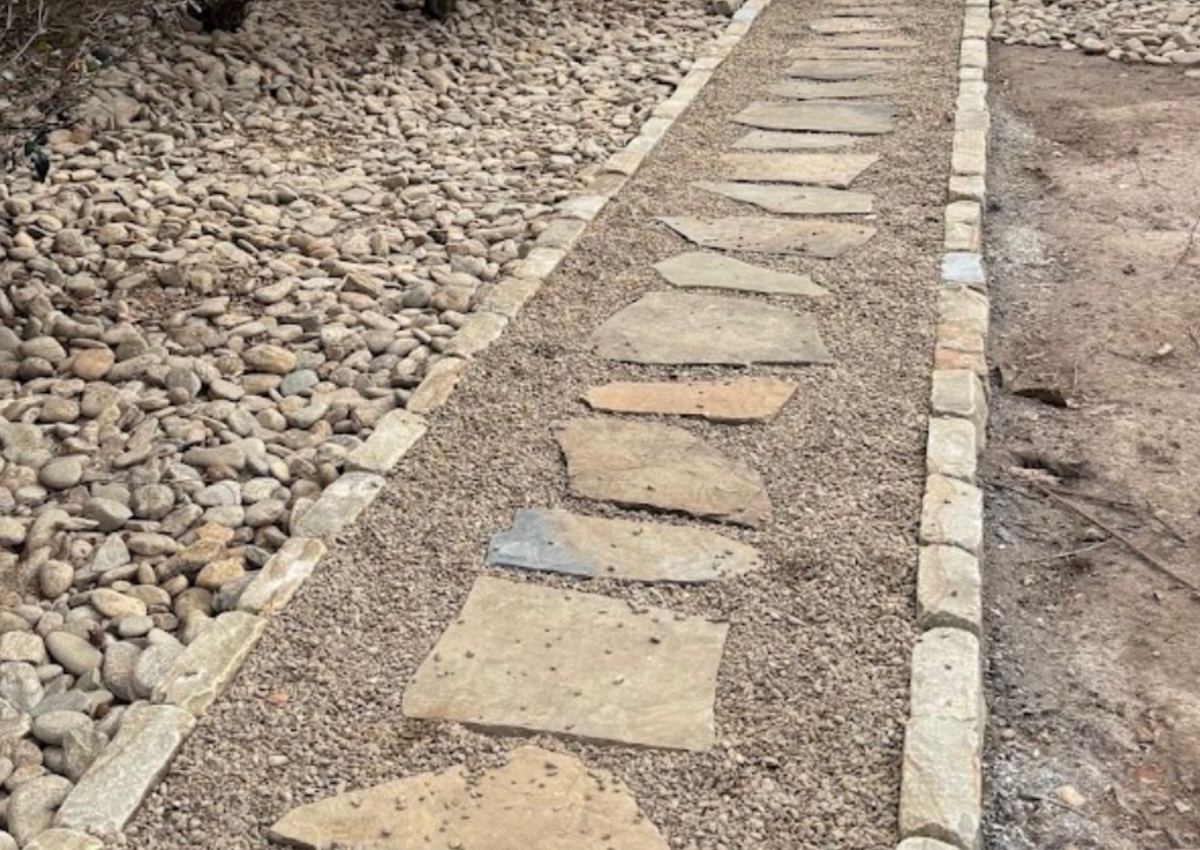 A stepping-stone path set into a river rock border alongside a house.