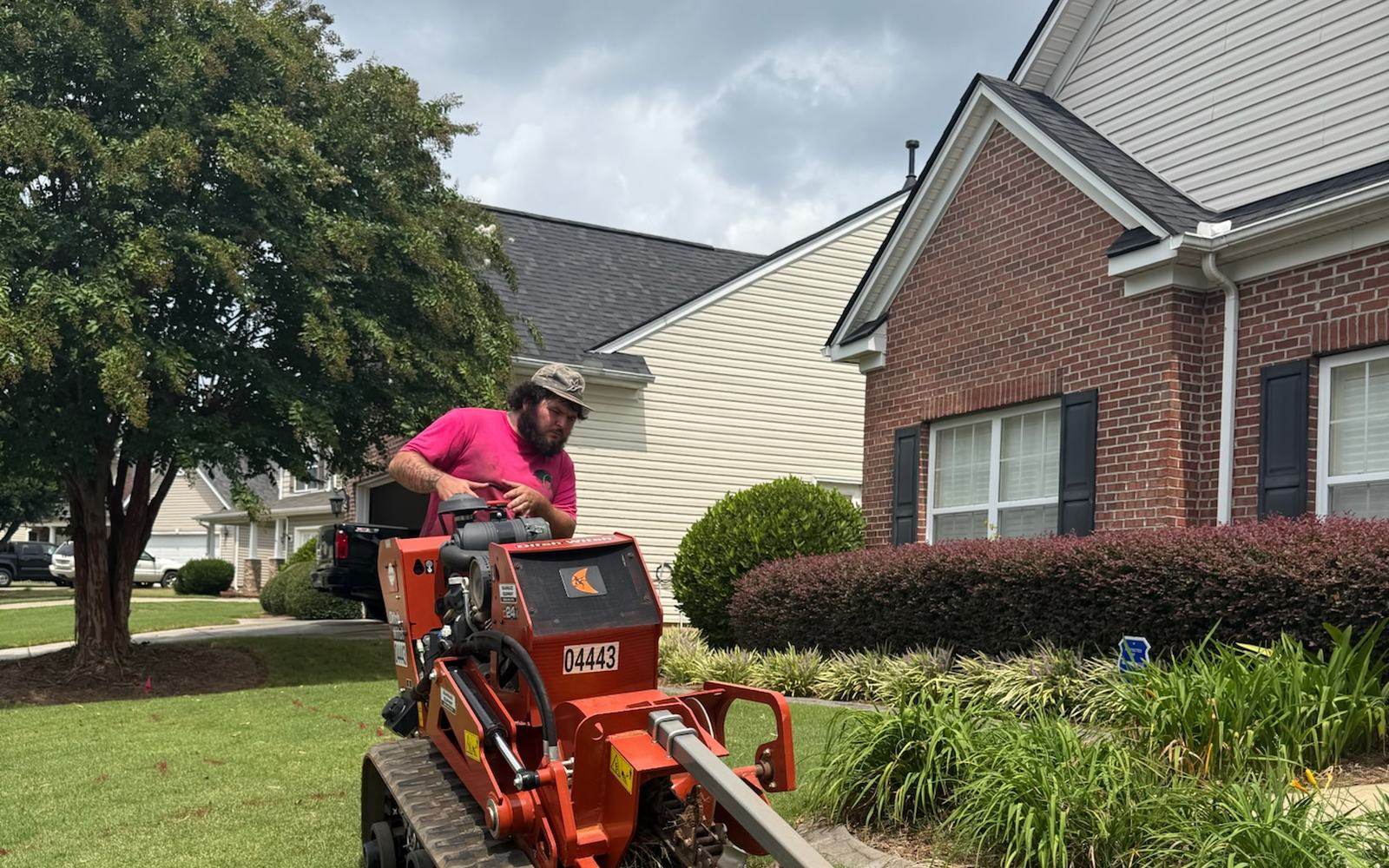 A crew member running a trencher to lay new irrigation line across a residential yard.