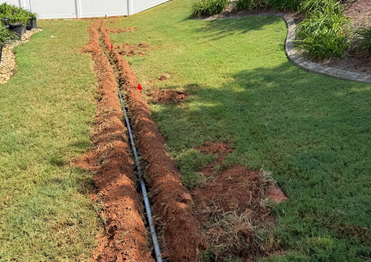 A trenched mainline with new irrigation pipe laid in it, running across a back lawn.