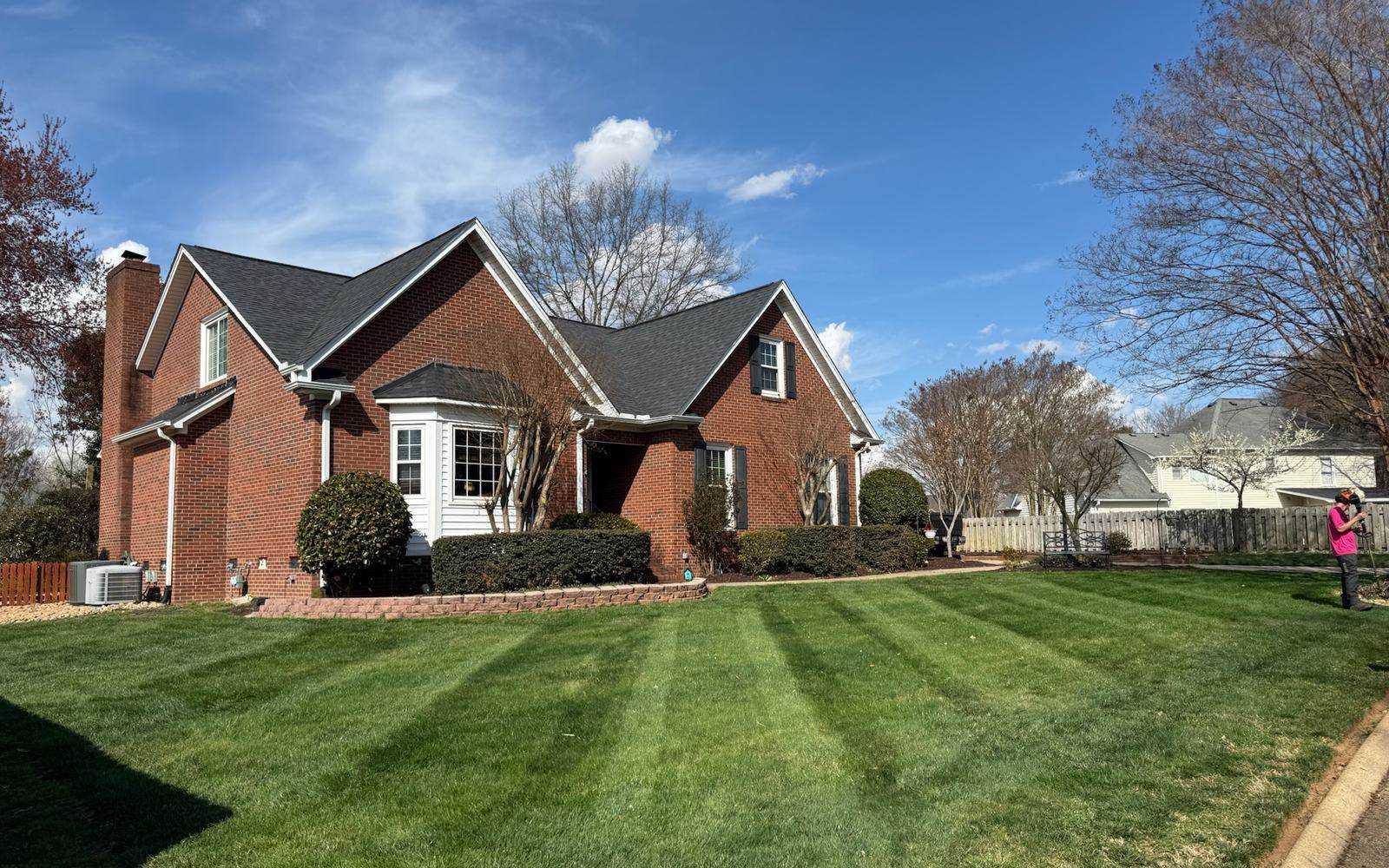 A striped front lawn running up to a brick home after a weekly cut.
