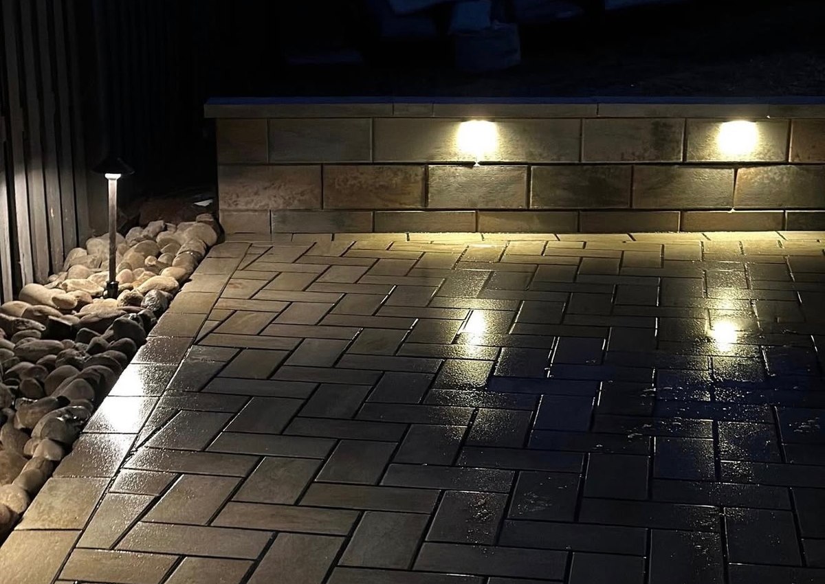 Lights set into a seating wall throwing pools of light across a paver patio.