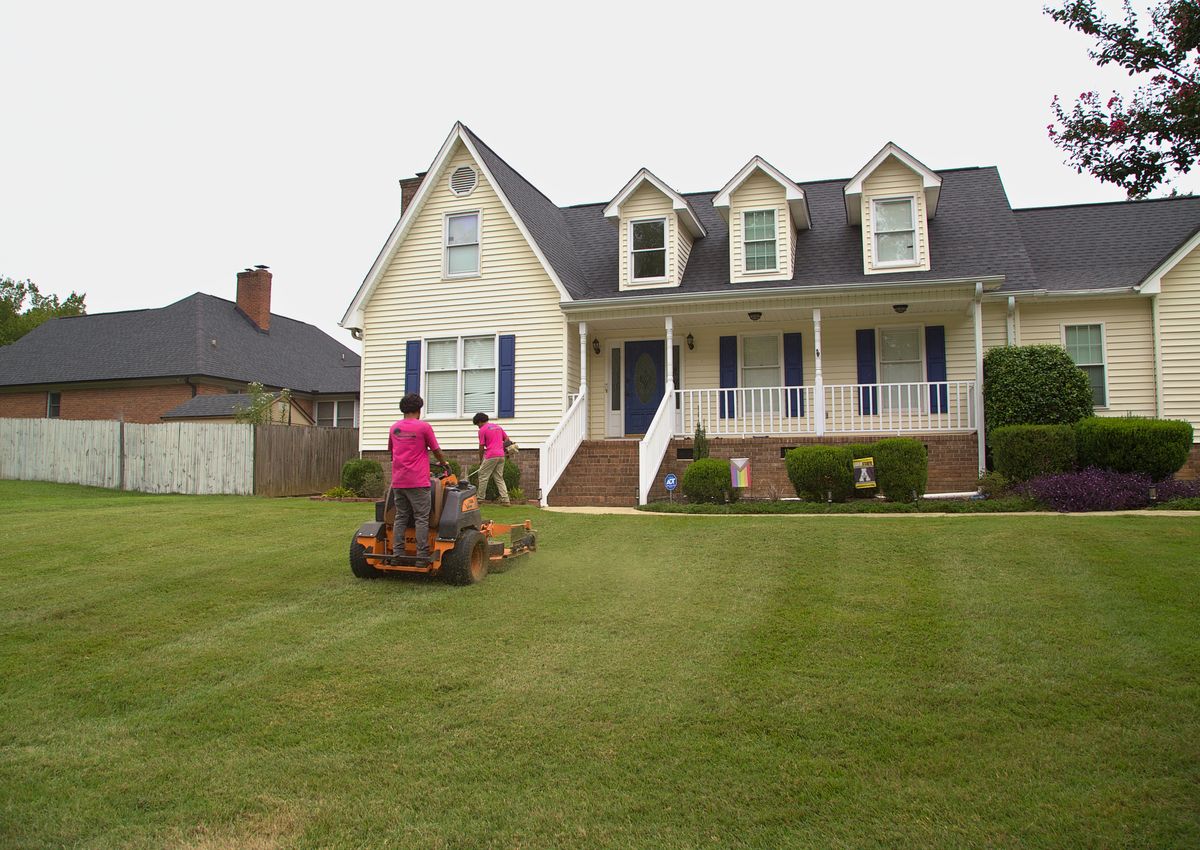 Mowing and trimming a striped front lawn at a home.