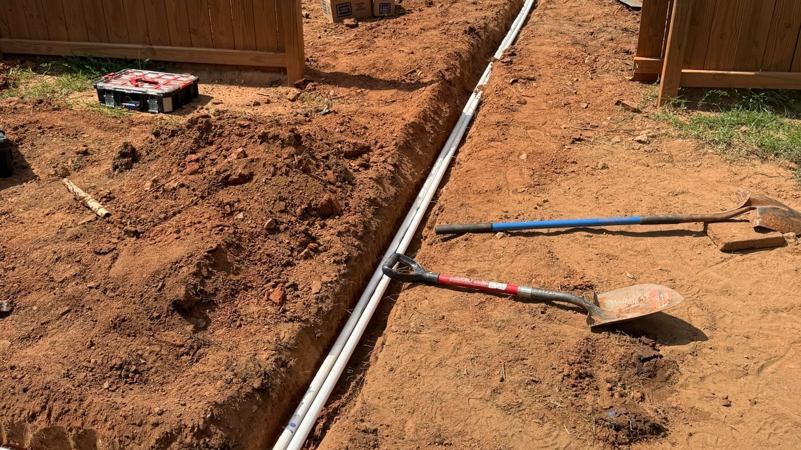 A trench run across a back yard with new irrigation line laid in it.