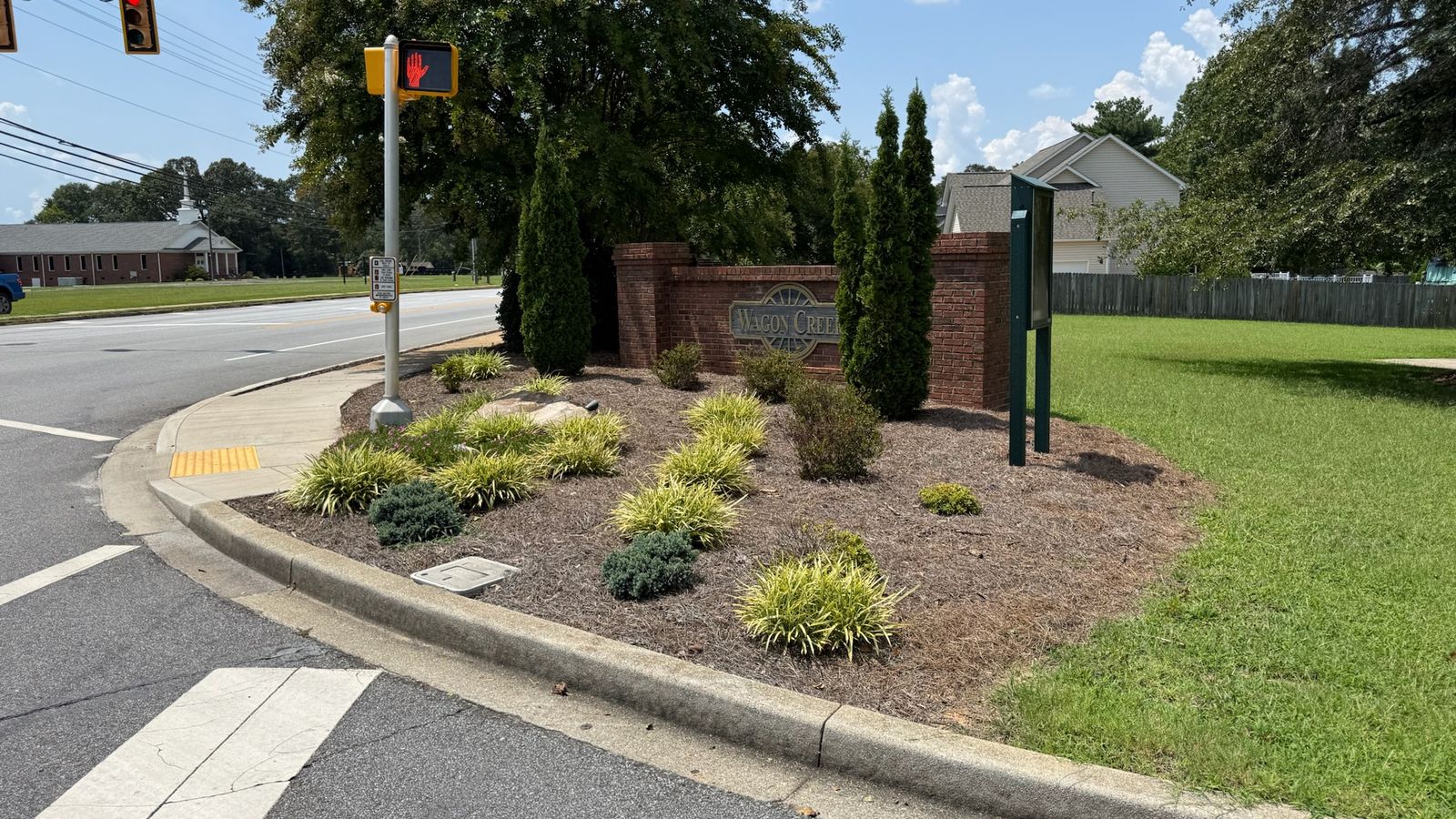 A landscaped commercial entrance island with shrubs and clean mulch beds at a street corner.