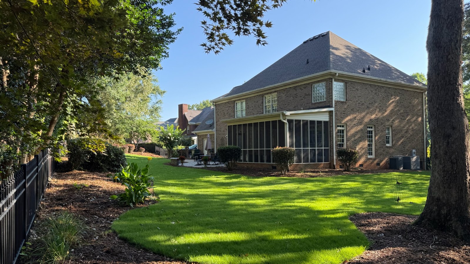 A maintained back lawn with edged mulch beds running along a brick home.