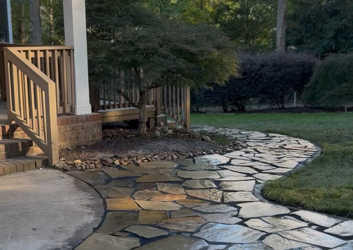 A flagstone walkway curving through a planted bed beside a covered porch, built on graded ground.