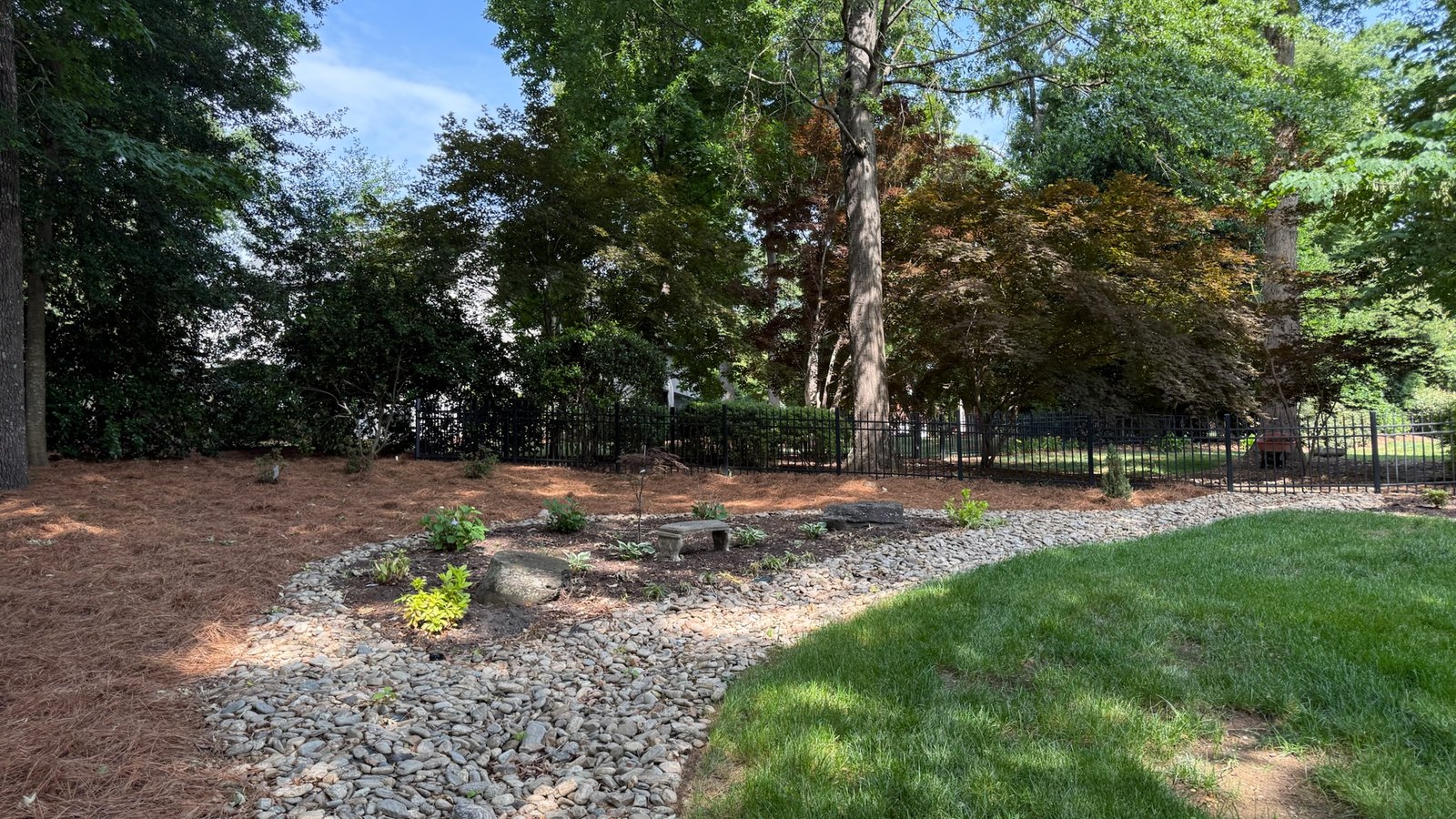 A river rock dry creek bed curving through a mulched bed beside a lawn.